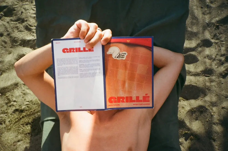 Personne allongée sur le sable lisant un cahier de mots fléchés GRILLÉ ouvert à la plage