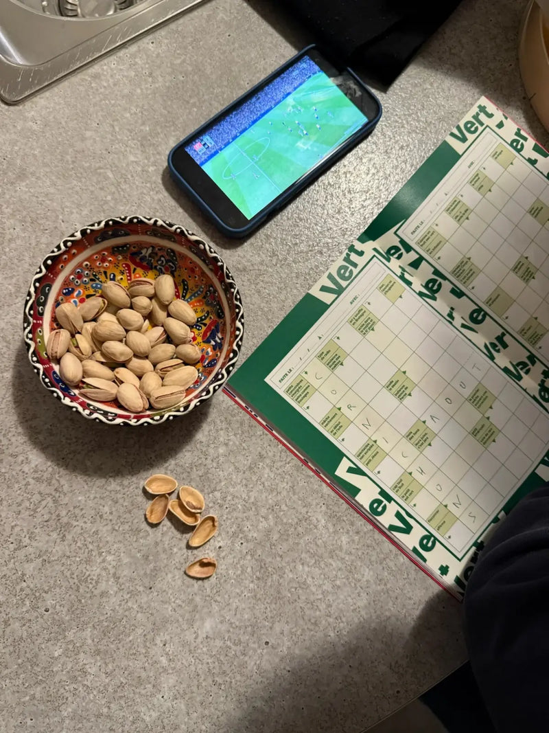 Cahier de mots fléchés GRILLÉ Vert ouvert avec pistaches et match de foot sur smartphone