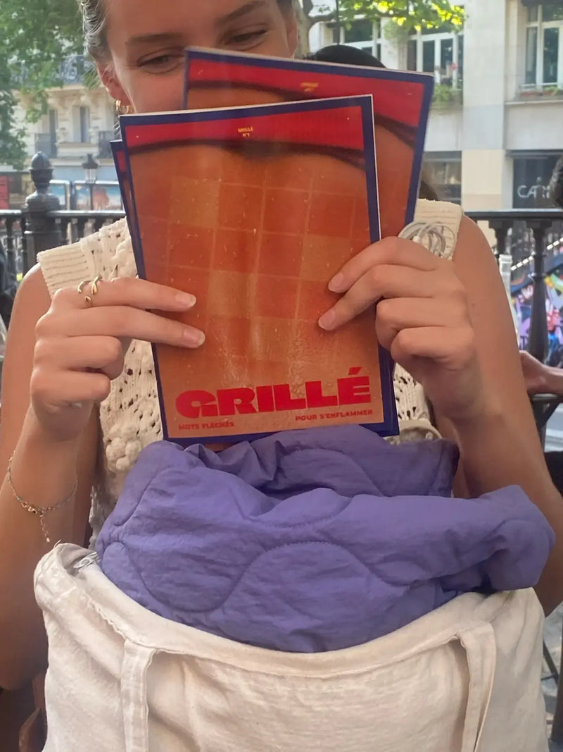 Femme tenant des cahiers de mots fléchés GRILLÉ niveau Chaud en terrasse parisienne